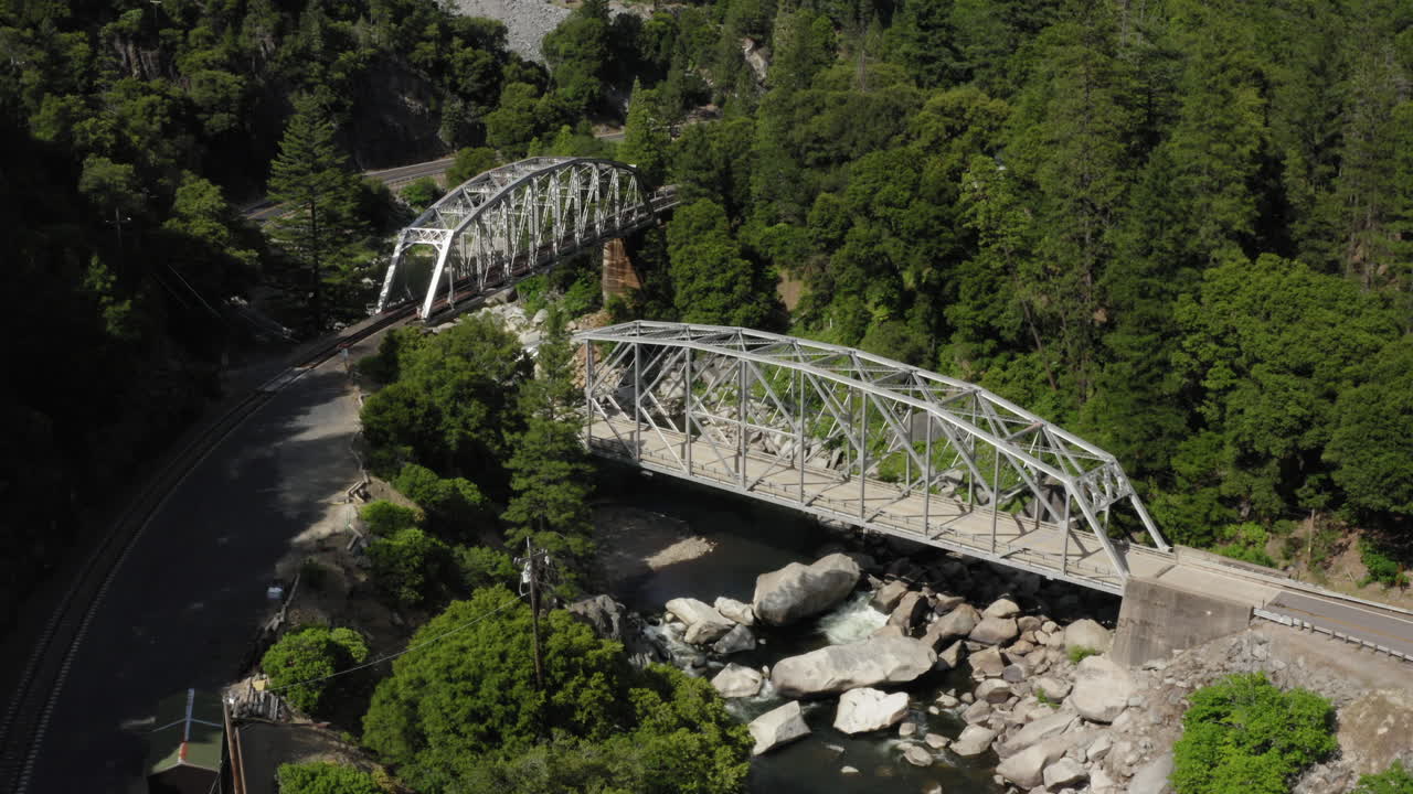 Two through arch bridges crossing river in National Forest, railroad bridge, highway 70 bridge, metal arch, aerial