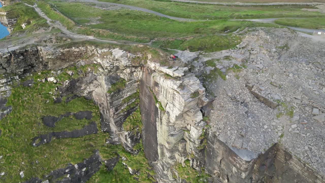드론은 해가 지는 동안 두 사람이 모허의 절벽에 앉아있는 동안 뒤로 날아갑니다.