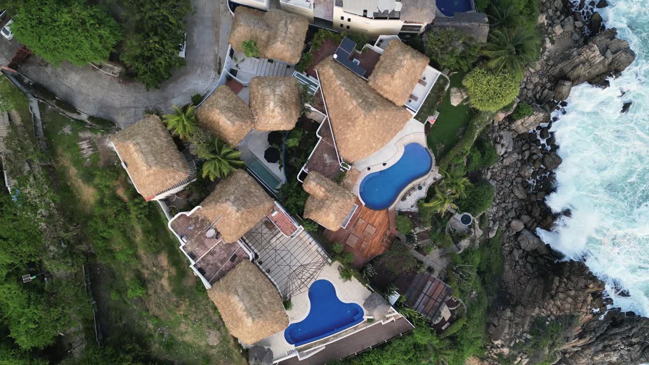 Drone captures the Oaxaca coastline, the ocean's force against the rocks and oceanfront residences at Puerto Escondido, Mexico