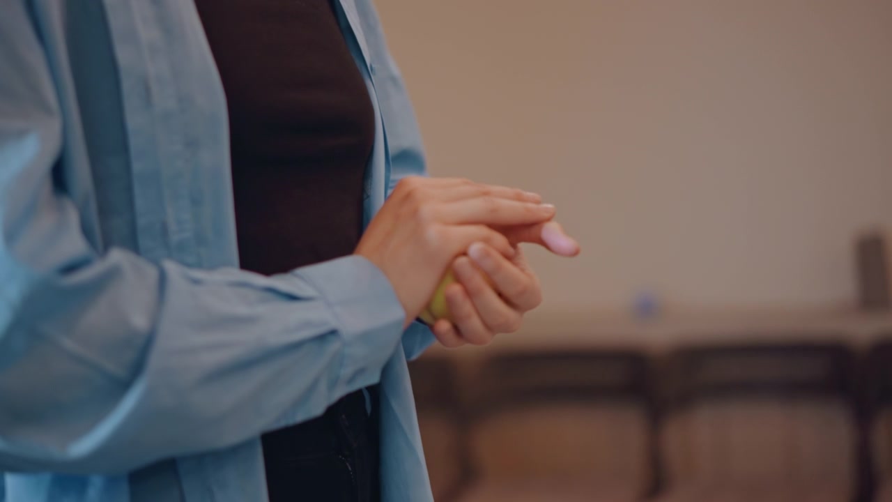 Mani che stringono una palla gialla in classe, istruttore di musica che dimostra esercizi di riscaldamento delle dita per strumentisti, tono didattico calmo con illuminazione soffusa, sedie e materiali per la pratica sfocati