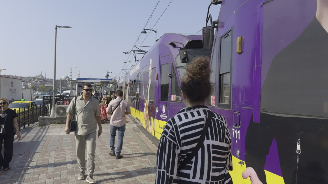 Person walking alongside a moving tram on Galata Bridge, with views of the city and waterfront in the background