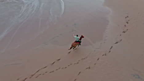 toma aérea de drones de un solo hombre montando a caballo galopando a lo largo de la playa en tambor, costa rica