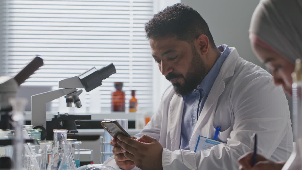 Scienziato che digita sullo smartphone alla scrivania in laboratorio