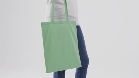 caucasian woman wearing white hoodie holding green bag on white background, copy space, slow motion