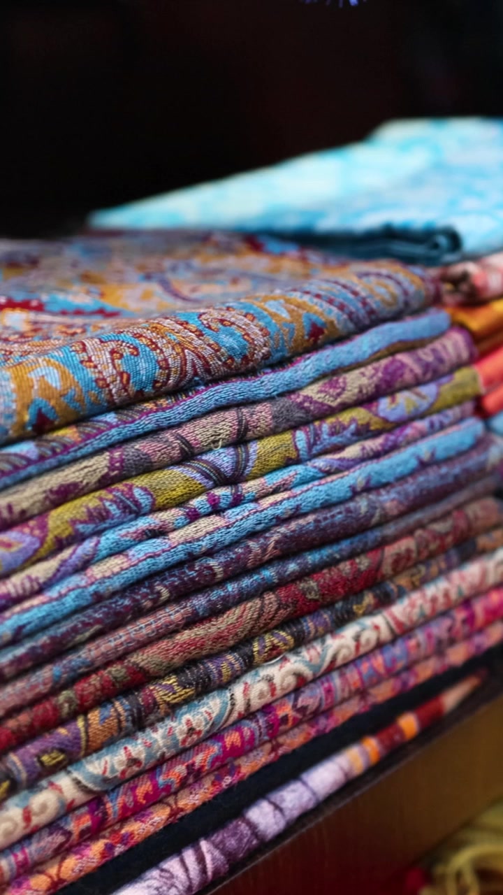A detailed vertical view of neatly stacked traditional fabrics with intricate patterns and vibrant colors.