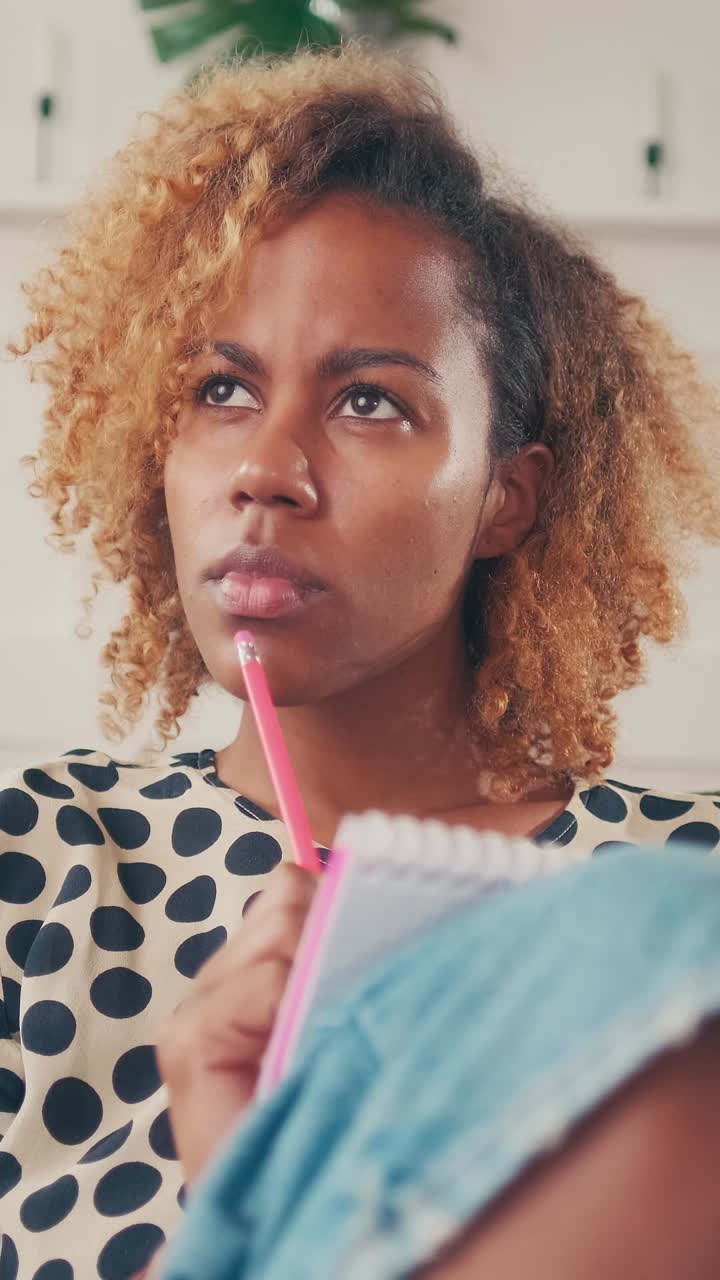 Giovane artista afroamericana disegna uno schizzo su un taccuino, seduta sul divano.