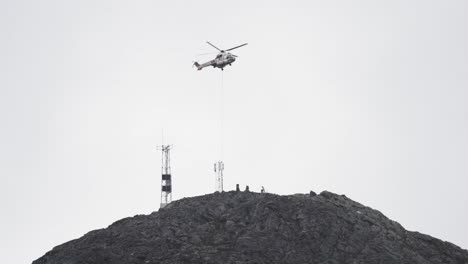 un helicóptero flota sobre un pico de montaña escarpado, ayudando en la instalación de equipos en una alta torre de radio