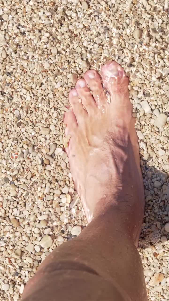 Piede che si erge in acque basse e limpide su una spiaggia di ciottoli