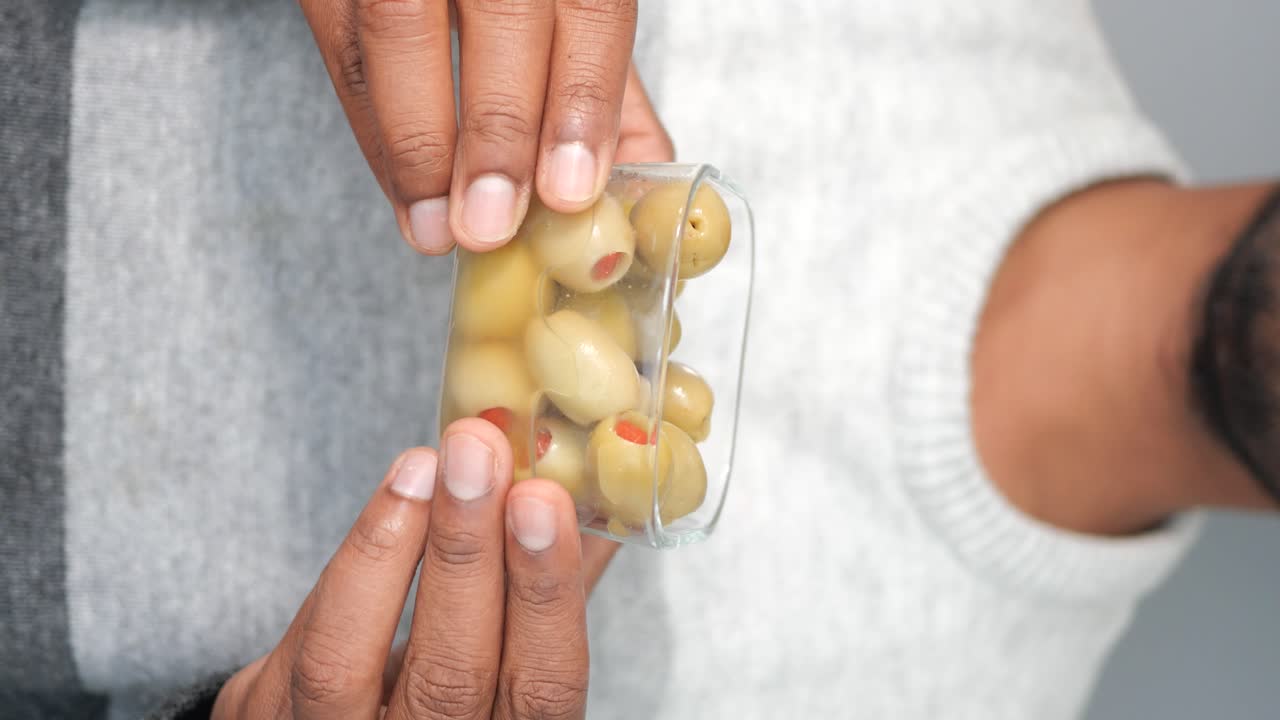 Hands holding a glass container of green olives