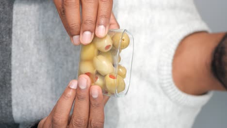 hands holding a glass container of green olives