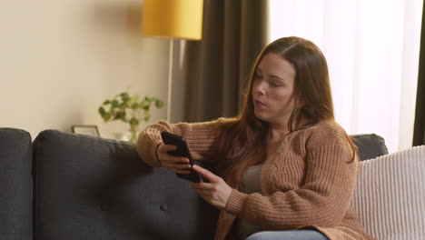 Woman-Sitting-On-Sofa-At-Home-Using-Mobile-Phone-To-Check-Social-Media-Message-And-Scrolling-Online-11