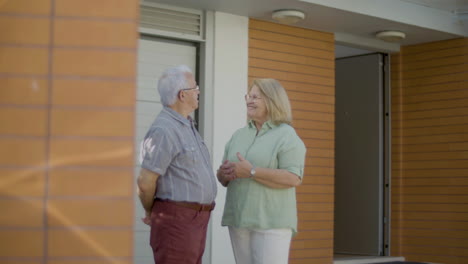 feliz casal sênior conversando em pé ao ar livre ao lado de sua nova casa