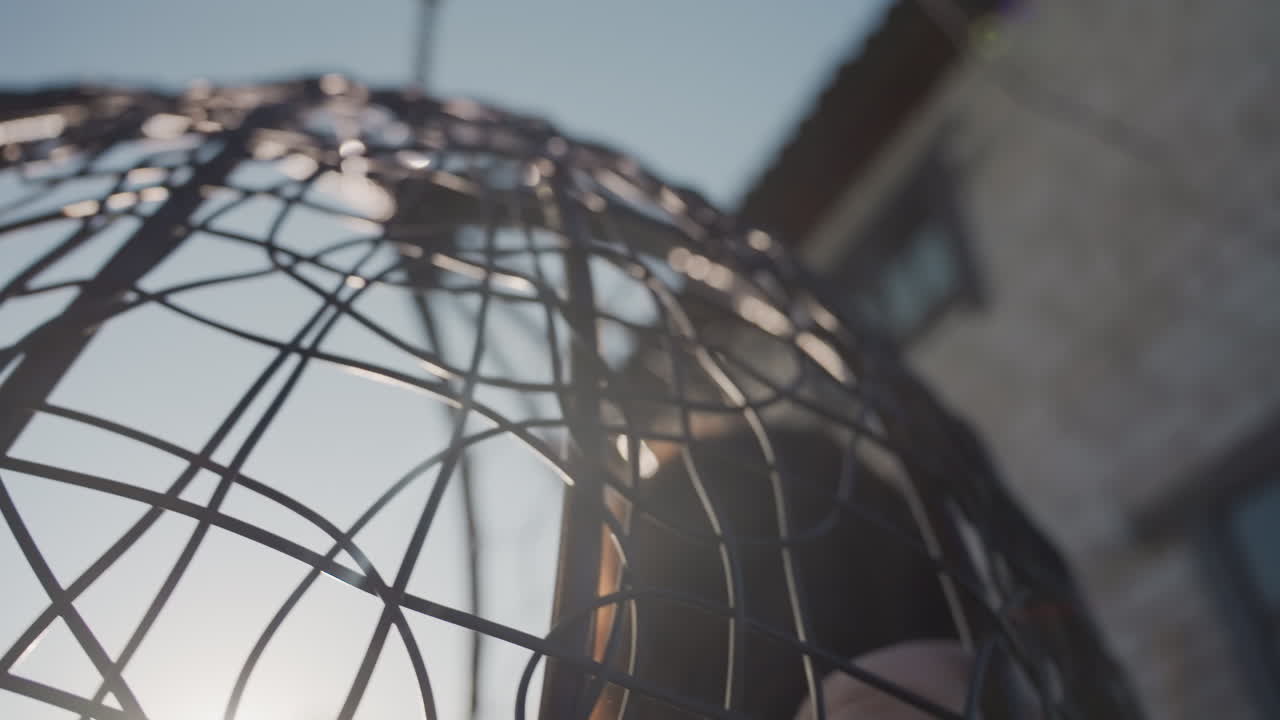Caucasian Silhouette With Intricate Metal, Dramatic Geometric Shapes Formed By Sunlight And Metal Pattern, Backyard Scene Featuring Sunlit Woven Cage And Detailed Metal Design Casting Textured Shadows