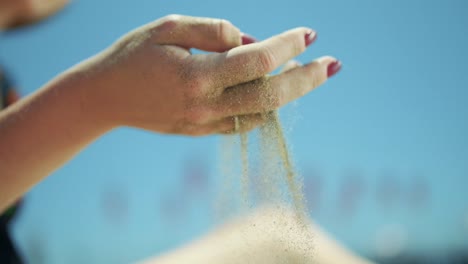 close-up slow motion image of beach sand pouring from woman's hand.