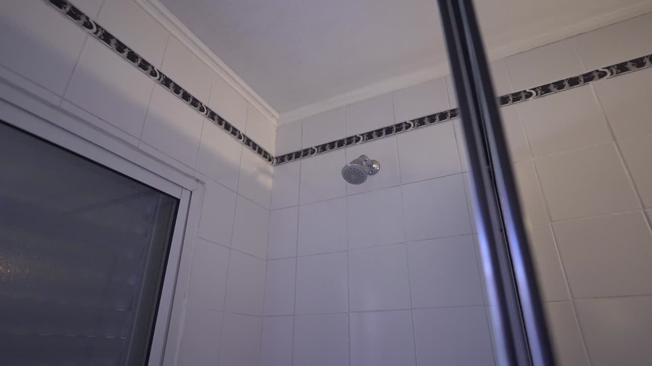 Shower head mounted on tiled house bathroom wall with rod and ceiling corner visible.