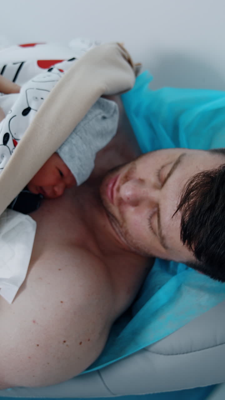 New father is holding his precious newborn child. Dad holds a baby skin to skin after birth. Top view. Vertical video