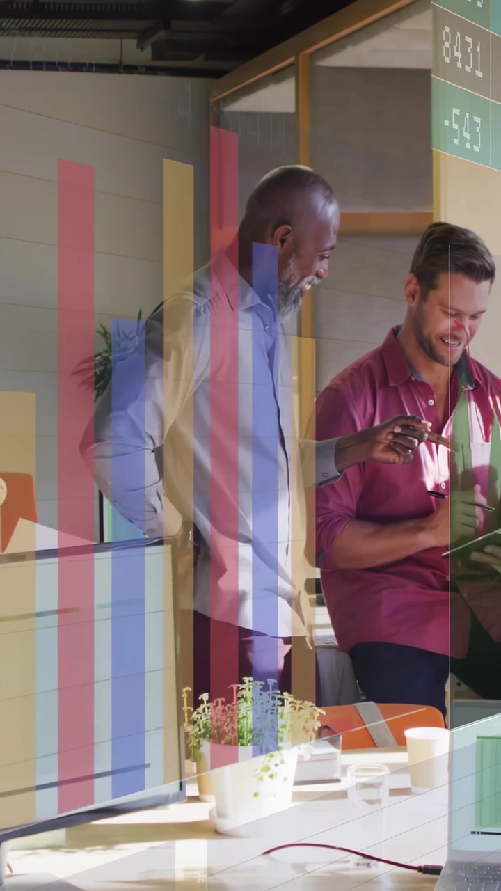 Video verticale: Toccando il tablet, un uomo con la maglia bordeaux guida un collega nella revisione di grafici in ufficio.