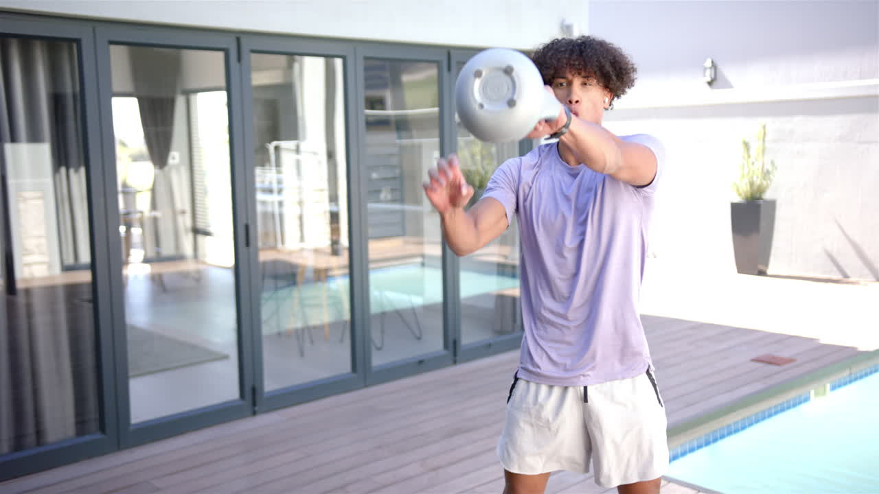 Exercising outdoors, man lifting kettlebell in backyard near swimming pool, copy space
