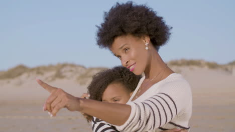 madre feliz abrazando y hablando con su linda hija en la playa