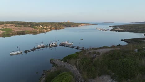 el dron desciende a lo largo de la pared de roca hasta el muelle de madera del puerto de barcos de pesca en sa nitja menorca, españa.