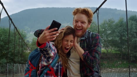 Friends-taking-selfie-photo-on-smartphone.-Tourists-couple-grimacing-at-mountain