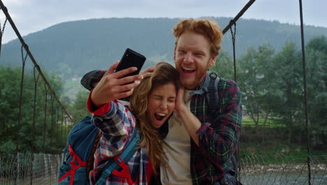 friends taking selfie photo on smartphone. tourists couple grimacing at mountain