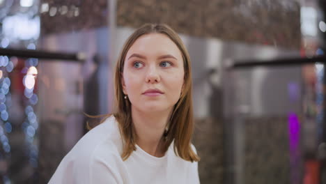 mujer joven sentada en el interior con una mirada contemplativa, rodeada de sutiles reflejos de luz azul y tonos cálidos en un espacio moderno
