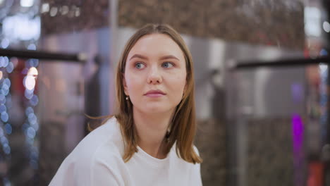 jovem sentada em casa com um olhar contemplativo, cercada por sutis reflexos de luz azul e tons quentes em um espaço moderno