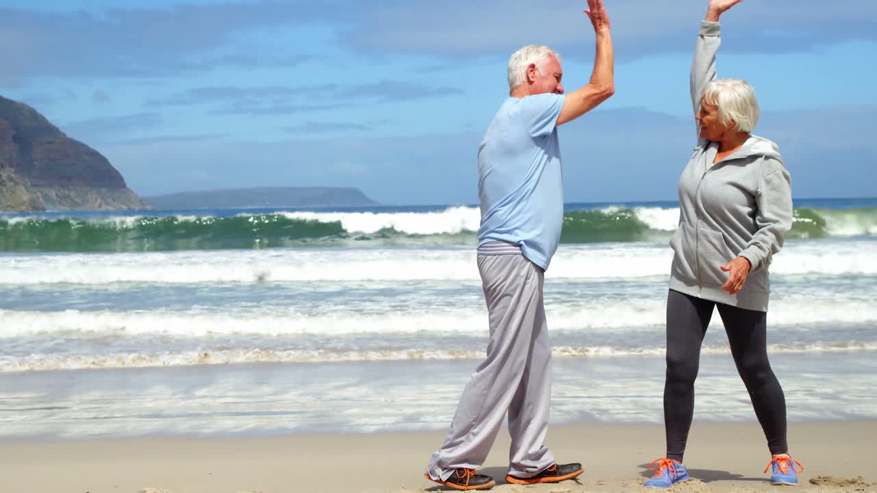 Pareja mayor chocando las cinco en la playa