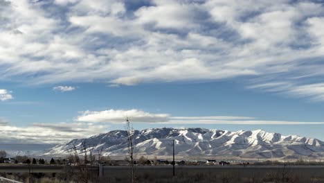 a busy highway in the foreground with a snowy mountain in the background and cloudscape overhead - panning time lapse