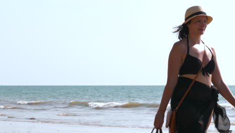 happy female tourist walks on tropical beach in thailand with waves in background