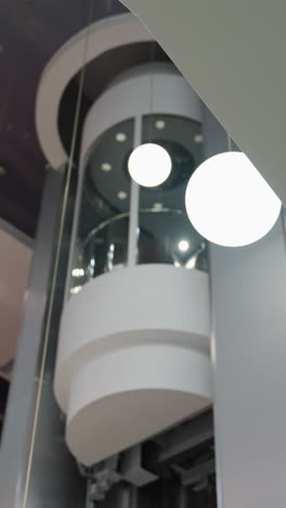 vista en primera persona capturando un ascensor con diseño moderno y lámparas redondas en el fondo. la cámara se centra en los elegantes elementos arquitectónicos y las esferas iluminadas