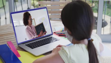 Kaukasisches-Schulmädchen-Mit-Gesichtsmaske,-Das-Einen-Laptop-Bei-Einem-Videoanruf-Mit-Einer-Lehrerin-Benutzt