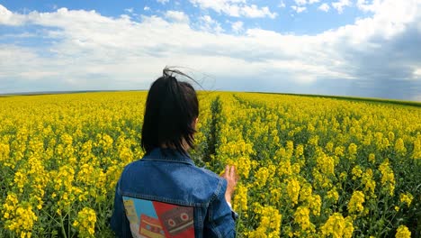 back view of a girl walking on the rapeseed farm in the countryside - slow motion