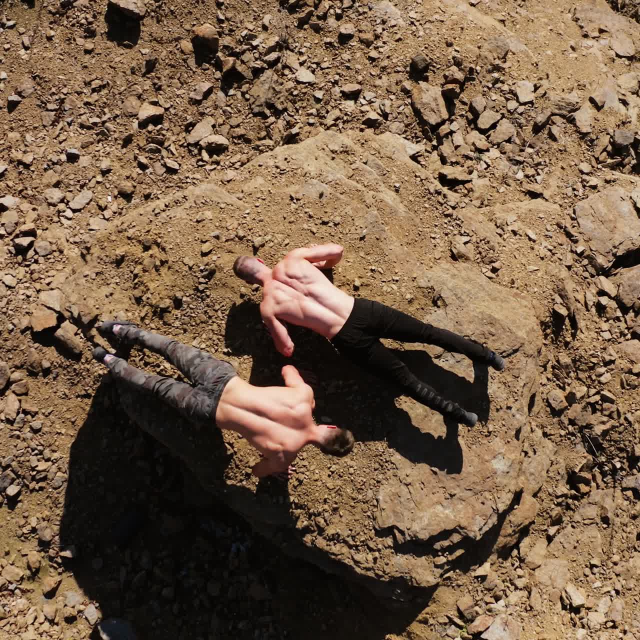 Top view on two sportsmen doing push-ups on rocks. Shirtless young athletes doing push ups on the hill in summer day. Aerial view.