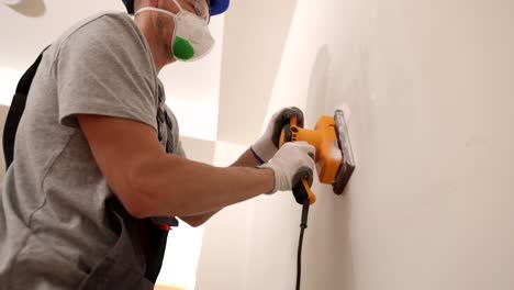 worker sanding a wall with an electric sander during home renovation