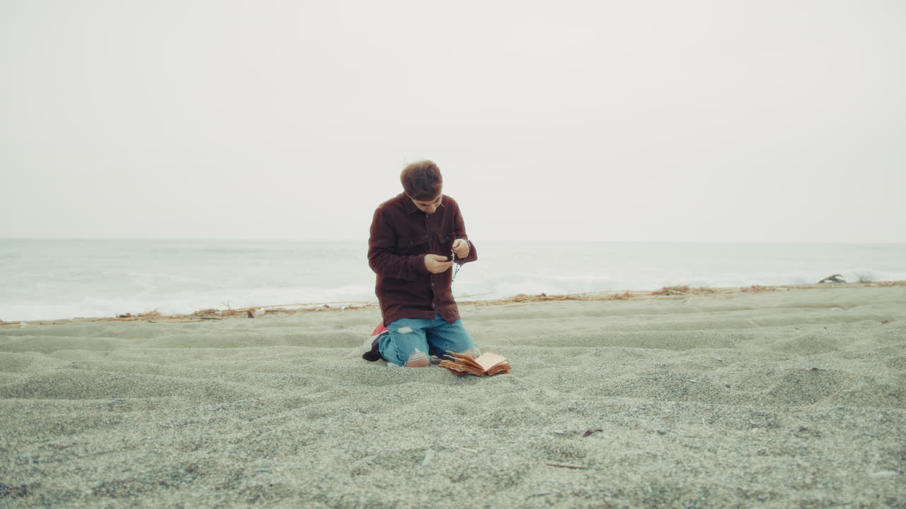 Faithful Man Praying God At The Sea On His Knees During Overcast Day