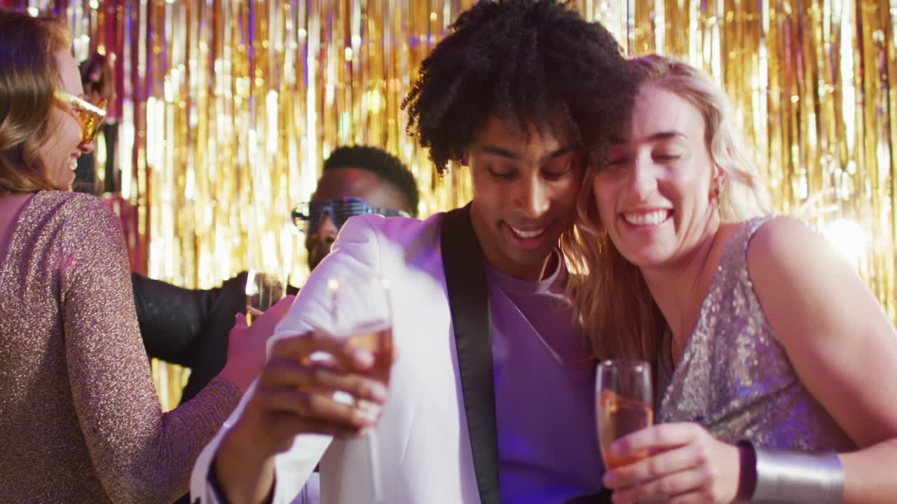 Video of happy diverse couple dancing holding glasses of champagne at a nightclub