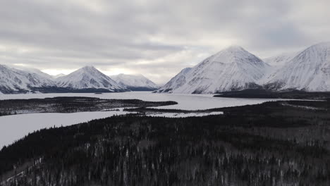 frozen kathleen lake surrounded by wintry mountains and fir trees at kluane national park in yukon, canada. aerial pullback shot