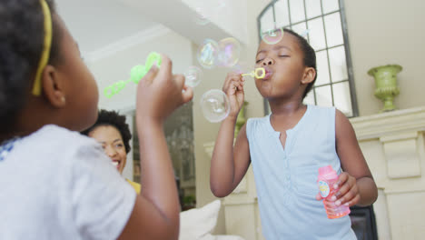 feliz abuela afroamericana con hija adulta y nietas soplando burbujas