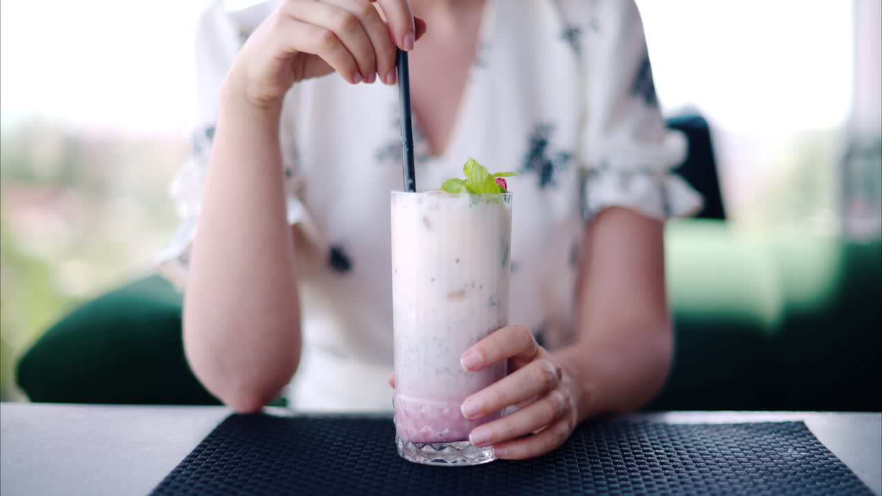 Woman mixing a strawberry drink with a black straw at a restaurant