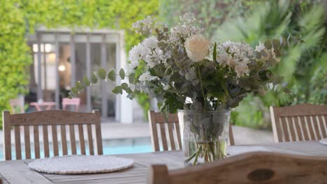 slow establishing shot of a bouquet of flowers on a table beside a pool at a villa