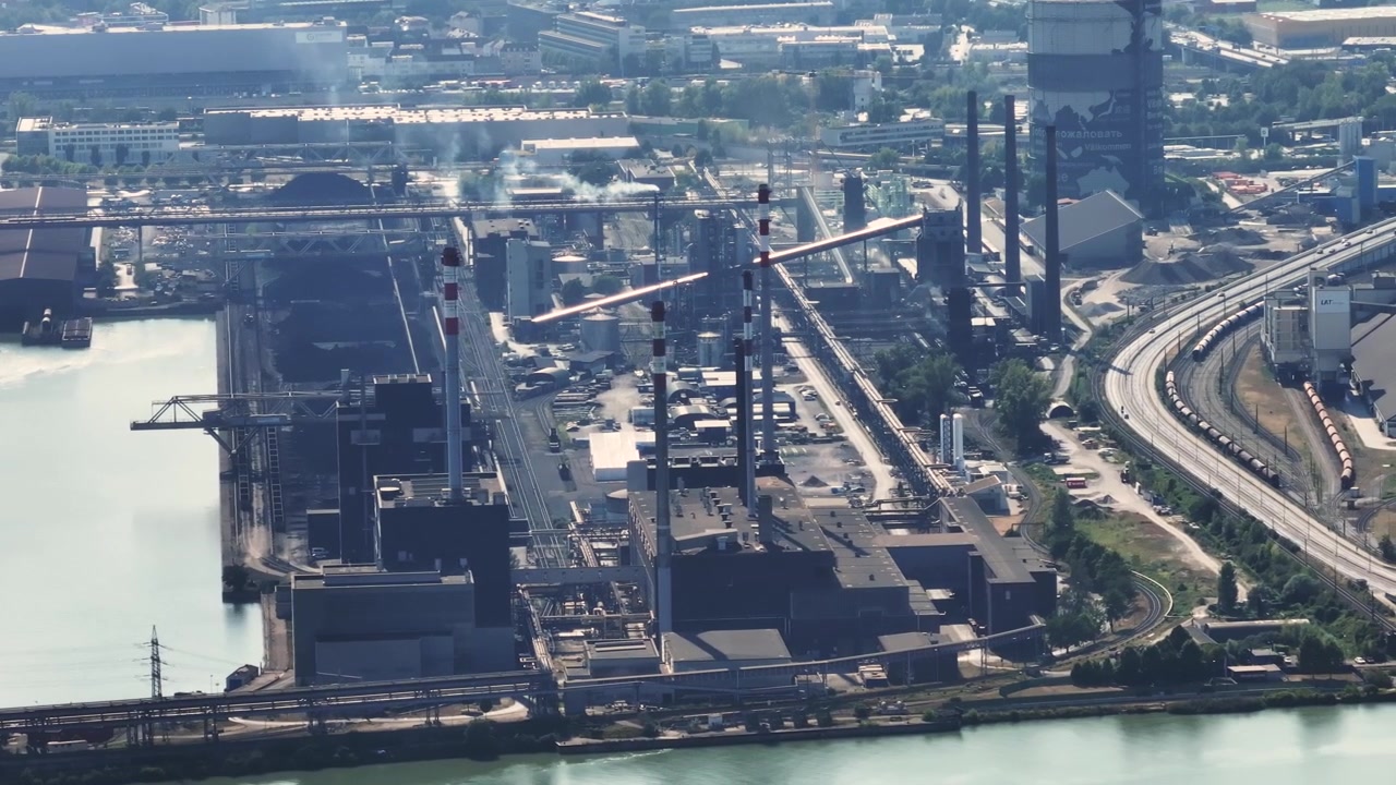 Expansive aerial view of a large steel manufacturing and metallurgical complex. Smokestacks are emitting smoke across the industrial zone