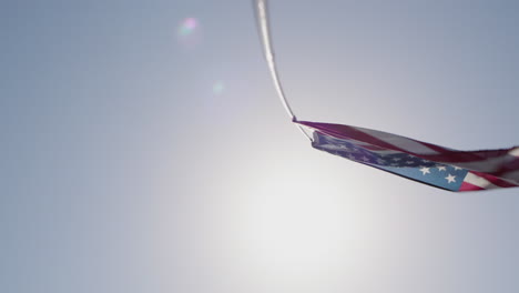 american flag waving on a pole against the blue sky and sun