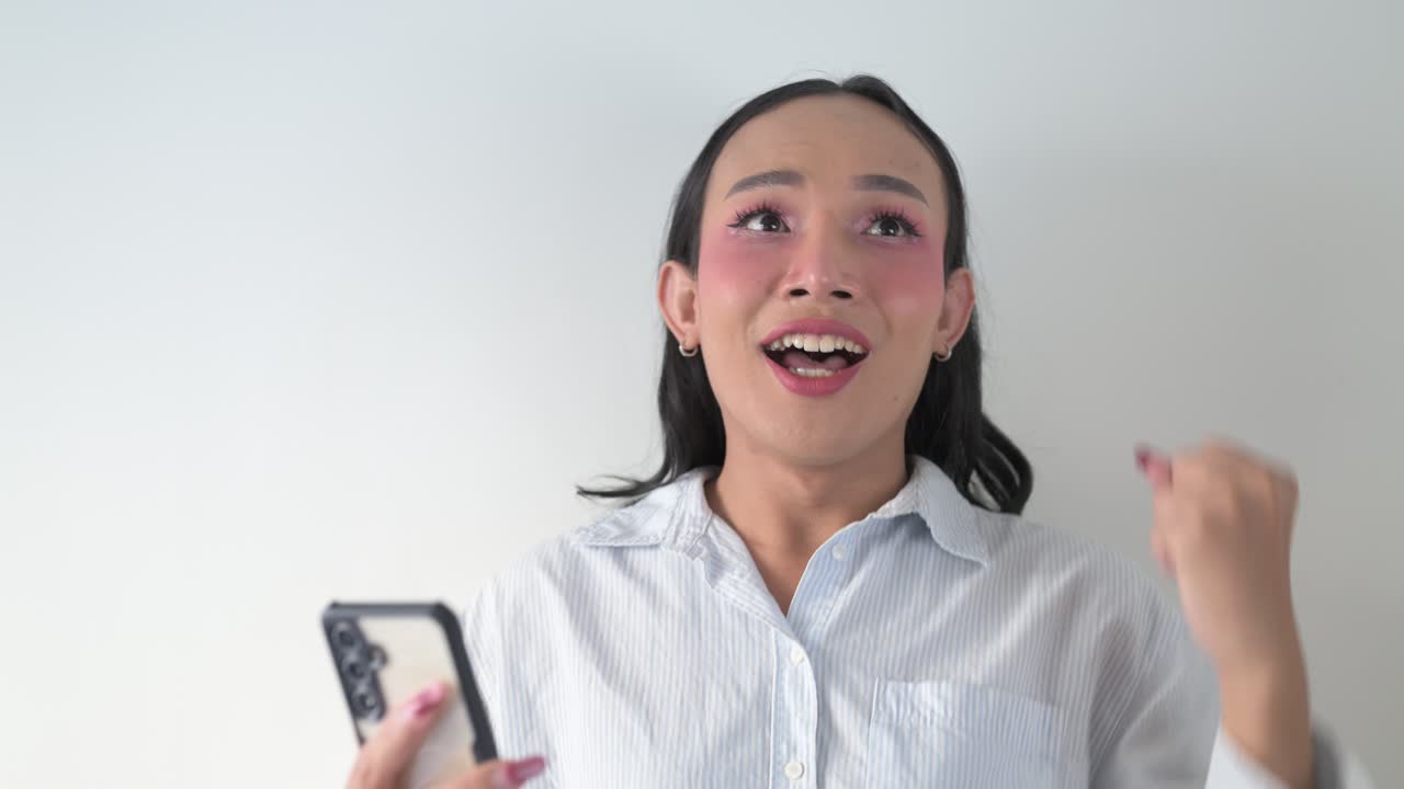 Thai transgender person using smartphone against white background wall indoors getting good news