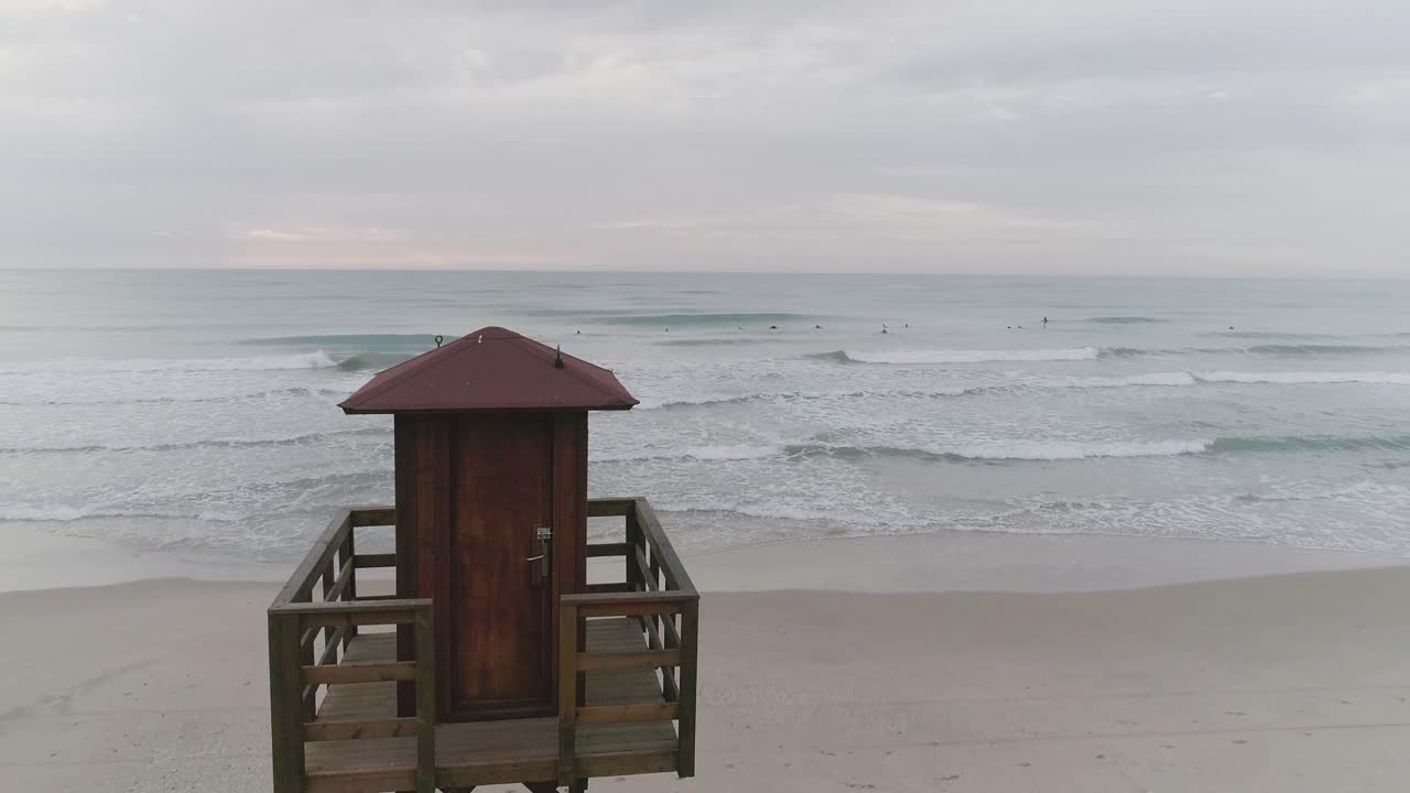 Rekaman melintas Menara Penjaga Pantai di pantai peselancar dengan peselancar di latar belakang