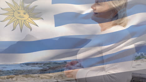 animation of flag of uruguay over happy senior caucasian woman on beach