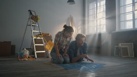 Focused-couple-planning-house-renovation-indoors.-Woman-pointing-to-blueprints.