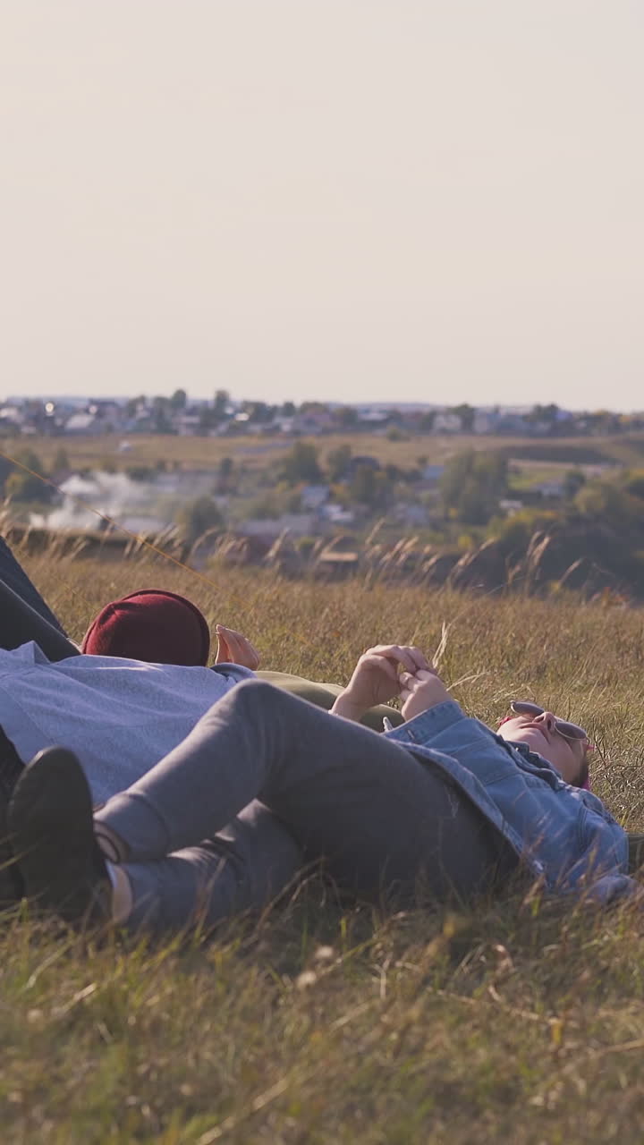 woman friends rest lying on dry brown grass near blue tent on high river bank against clear sky in autumn evening