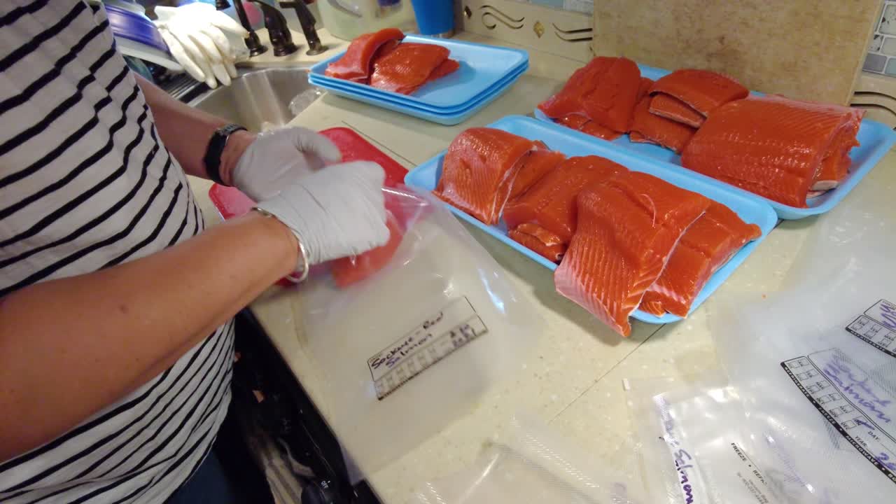 manos enguantadas poniendo filetes de salmón sockeye frescos en bolsas de plástico para ser sellados al vacío más tarde